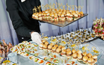 Waiter with meat dish serving catering table with food snacks